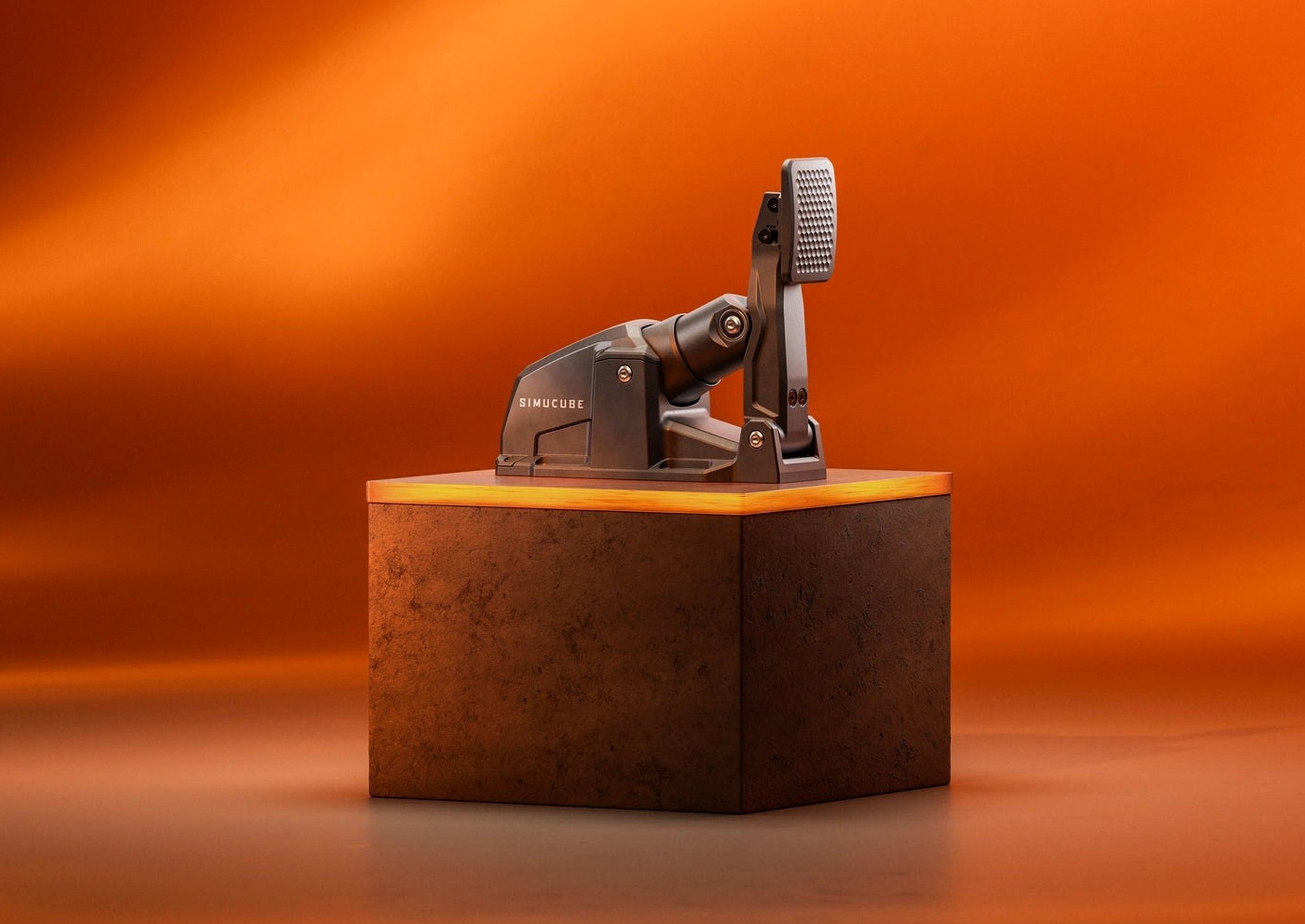 La pédale active Simucube ActivePedal Sport posée sur un socle, devant un fond orange